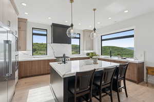 Kitchen featuring modern cabinets, high quality fridge, light wood-style floors, a kitchen island with sink, and recessed lighting