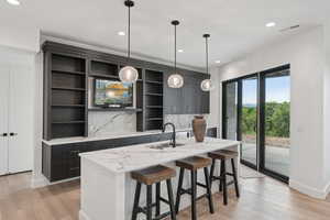 Kitchen featuring open shelves, a center island with sink, tasteful backsplash, light wood-type flooring, and pendant lighting
