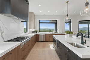 Kitchen with appliances with stainless steel finishes, light wood-type flooring, recessed lighting, light stone counters, and backsplash