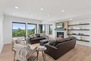 Living room featuring recessed lighting, a warm lit fireplace, and light wood-type flooring
