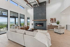 Living room featuring a towering ceiling, a premium fireplace, a chandelier, beamed ceiling, and wood finished floors