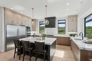 Kitchen featuring appliances with stainless steel finishes, light stone countertops, light wood-style flooring, decorative backsplash, and recessed lighting