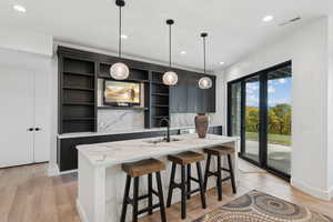 Kitchen with a breakfast bar, light stone counters, dark cabinets, decorative light fixtures, and recessed lighting