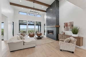 Living area with a high ceiling, wood finished floors, a high end fireplace, plenty of natural light, and beam ceiling