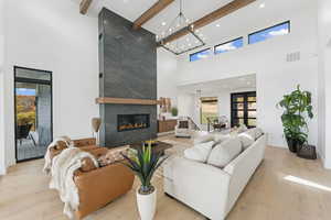 Living area featuring light wood finished floors, a fireplace, beamed ceiling, a towering ceiling, and recessed lighting