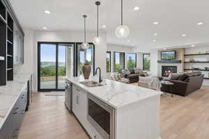 Kitchen featuring open shelves, stainless steel appliances, recessed lighting, an island with sink, and light wood finished floors