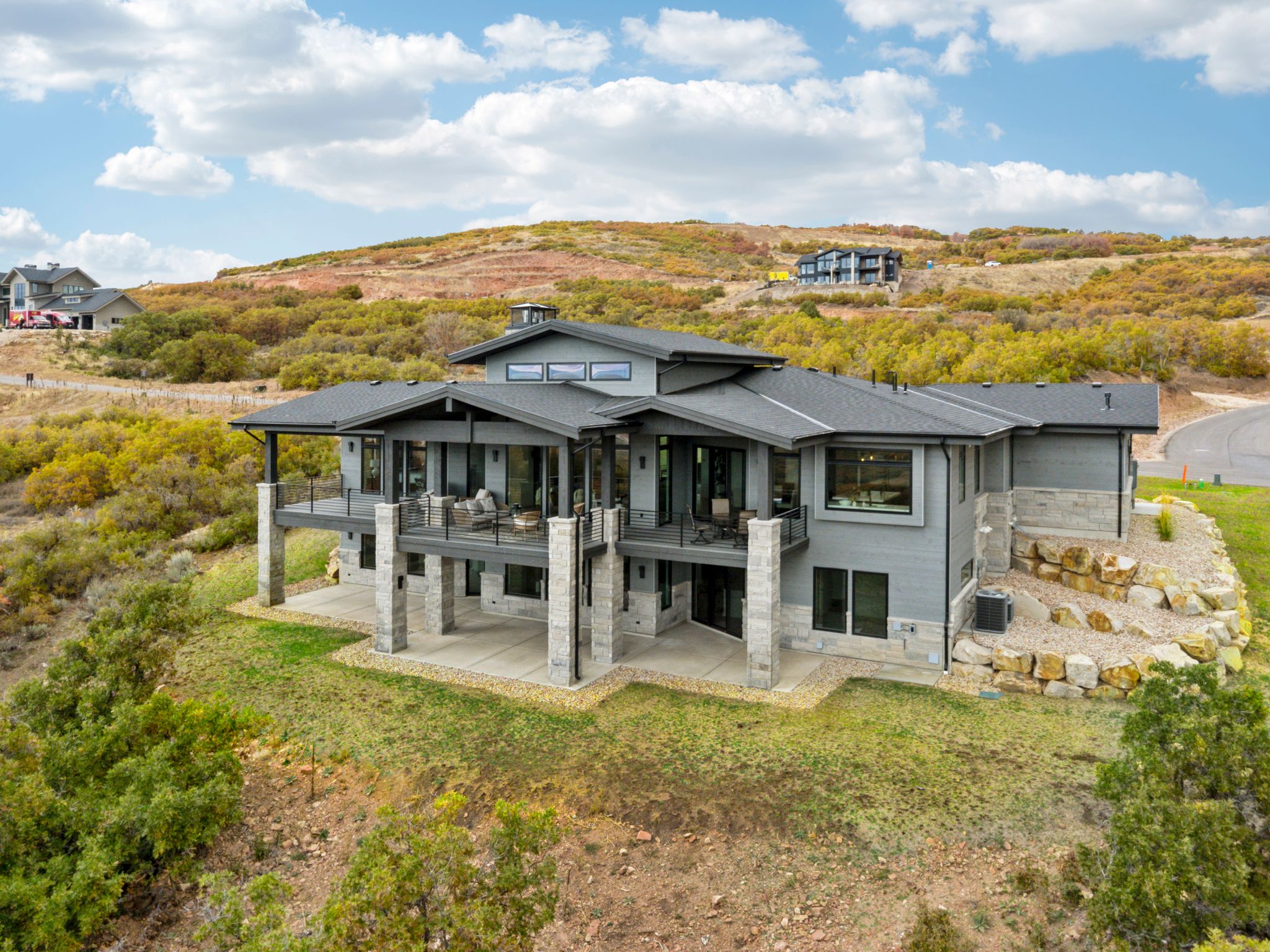 Back of house with a patio, stone siding, a shingled roof, and a lawn