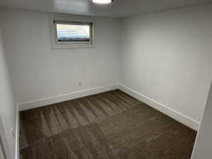Unfurnished room featuring dark colored carpet and baseboards