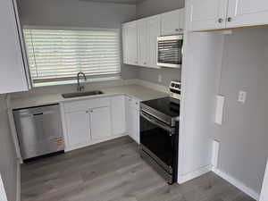 Kitchen with appliances with stainless steel finishes, light wood finished floors, white cabinets, and light countertops