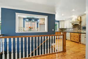 Kitchen with tasteful backsplash, stainless steel microwave, light wood finished floors, dark countertops, and ornamental molding