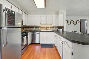 Kitchen with appliances with stainless steel finishes, a peninsula, dark countertops, a textured ceiling, and light wood-style floors