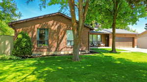 View of front of home featuring an attached garage, brick siding, a front lawn, and concrete driveway