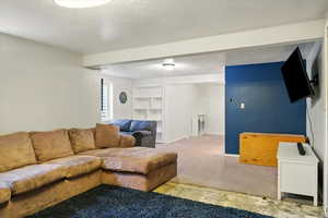 Living area featuring carpet flooring, built in shelves, and a textured ceiling