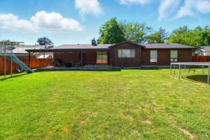 Rear view of house featuring a trampoline, a fenced backyard, a patio, brick siding, and a chimney