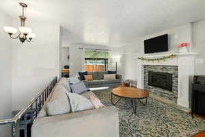 Living area with a textured ceiling, a chandelier, a stone fireplace, and wood finished floors
