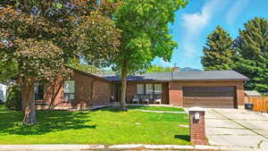 Ranch-style home featuring a garage, driveway, brick siding, and a chimney