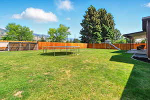 Fenced backyard featuring a trampoline, a playground, and a mountain view