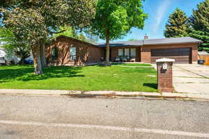 Ranch-style house featuring an attached garage, brick siding, concrete driveway, a front yard, and a chimney