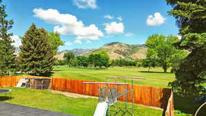 Fenced backyard with a mountain view, a trampoline, golf course view, and a playground