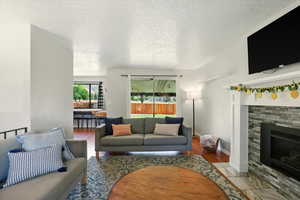 Living room with a textured ceiling, a fireplace with flush hearth, and wood finished floors