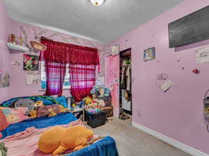 Carpeted bedroom featuring a closet, a textured ceiling, and a walk in closet