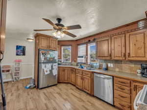Kitchen with appliances with stainless steel finishes, light wood-style floors, a ceiling fan, brown cabinets, and a textured ceiling