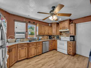 Kitchen with stainless steel appliances, under cabinet range hood, light wood-style floors, brown cabinets, and a textured ceiling