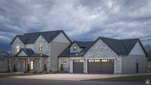 View of front facade with stone siding, a garage, driveway, and a standing seam roof