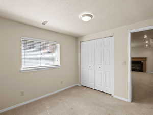 Unfurnished bedroom featuring light carpet, a closet, a fireplace, and a textured ceiling