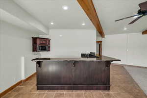 Kitchen with stainless steel microwave, a breakfast bar area, dark stone countertops, ceiling fan, and beam ceiling