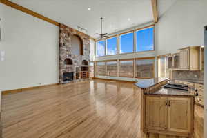 Living area featuring a ceiling fan, light wood-style flooring, a stone fireplace, a towering ceiling, and recessed lighting