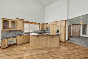 Kitchen featuring stainless steel microwave, high vaulted ceiling, light wood-style flooring, light brown cabinetry, and tasteful backsplash