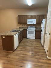 Kitchen with white appliances, a peninsula, light wood-type flooring, a textured ceiling, and brown cabinetry
