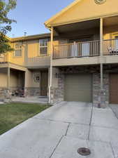 View of front facade with a balcony, stone siding, stucco siding, a garage, and driveway