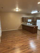 Kitchen featuring white appliances, a textured ceiling, a peninsula, wood finished floors, and open floor plan