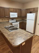 Kitchen featuring white appliances, a peninsula, light wood-style flooring, and brown cabinetry