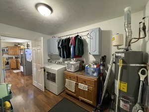 Washroom featuring strapped water heater, independent washer and dryer, dark wood-style flooring, a textured ceiling, and cabinet space