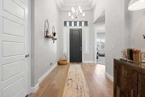 Foyer entrance featuring light wood-type flooring, a chandelier, a raised ceiling, and crown molding