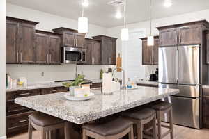 Kitchen with appliances with stainless steel finishes, a kitchen breakfast bar, dark brown cabinets, light wood finished floors, and an island with sink