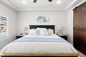 Bedroom featuring multiple windows, a barn door, recessed lighting, a raised ceiling, and a ceiling fan