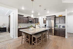 Kitchen featuring stainless steel appliances, dark brown cabinetry, light wood-style floors, a kitchen breakfast bar, and a kitchen island with sink