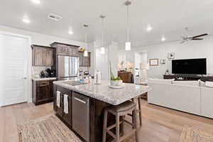 Kitchen with stainless steel appliances, light wood-style floors, dark brown cabinetry, open floor plan, and ceiling fan