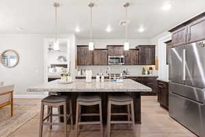 Kitchen with appliances with stainless steel finishes, dark brown cabinets, a kitchen bar, light wood-style floors, and recessed lighting