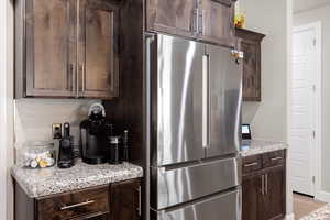 Kitchen featuring freestanding refrigerator, dark brown cabinetry, backsplash, light stone counters, and light wood-style floors