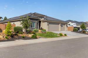 Prairie-style house featuring an attached garage, stucco siding, a tile roof, driveway, and stone siding
