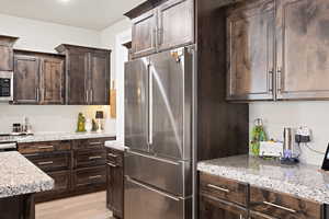 Kitchen with appliances with stainless steel finishes, dark brown cabinets, light stone countertops, and light wood-type flooring