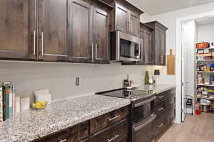 Kitchen featuring stainless steel appliances, dark brown cabinets, light stone counters, and light wood finished floors
