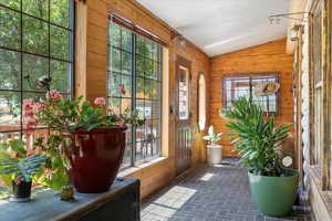 Doorway featuring wooden walls, lofted ceiling, and brick patterned floors