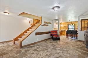 Living area featuring a textured ceiling, wooden walls, stone tile flooring, and stairs