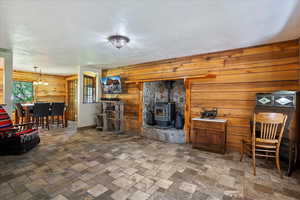 Living area featuring wood walls, a chandelier, a wood stove, a textured ceiling, and stone tile flooring